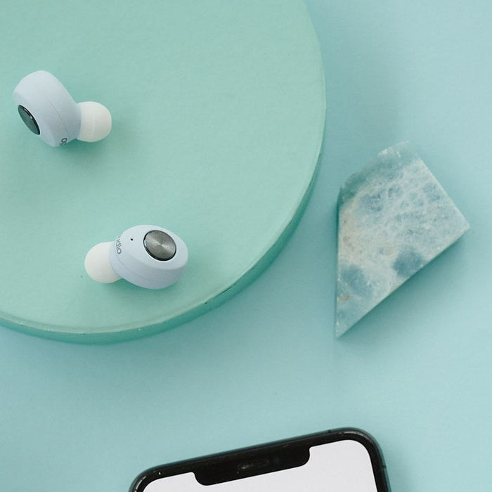 Wireless earbuds beside a smartphone on a blue background — cross-platform earbuds for Android and iPhone.