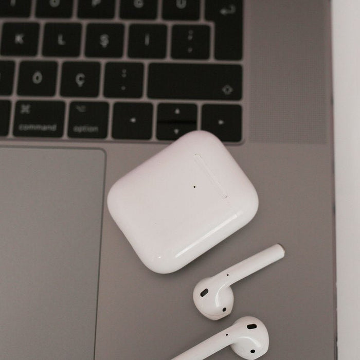Wireless earbuds and charging case on a laptop — spatial audio listening across phones, tablets, and computers
