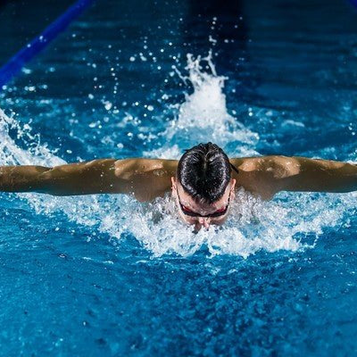 Professional swimmer doing freestyle in a pool with water splashing — best waterproof earbuds 2026 test scene