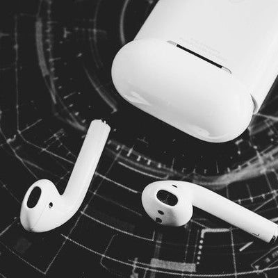 White wireless earbuds with charging case on dark textured background with high-contrast monochrome photography — true wireless TWS earbud product photography showing precision electronics aesthetic.