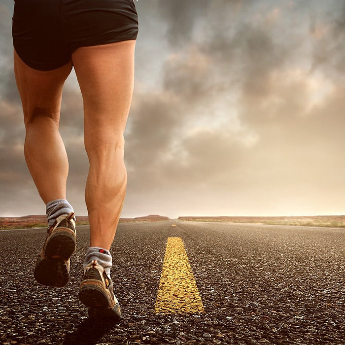 Runner's legs from behind on asphalt road at golden hour