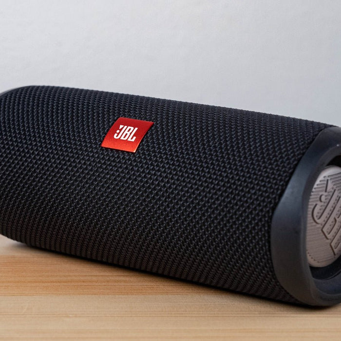 A black cylindrical portable Bluetooth speaker on a light wooden table